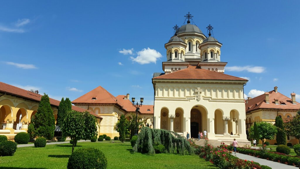 Romanian Orthodox cathedral with twin domes, arched portico, and manicured garden courtyard in Alba Iulia, Romania.
