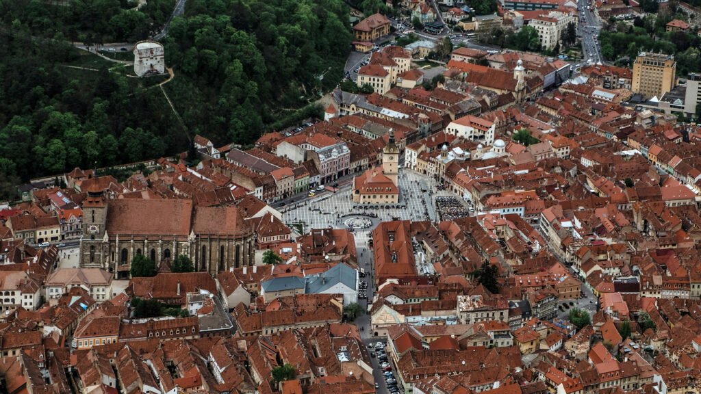 Aerial view of Brașov’s Old Town with red tile rooftops, the Black Church, and Council Square surrounded by historic buildings in Brașov, Romania.