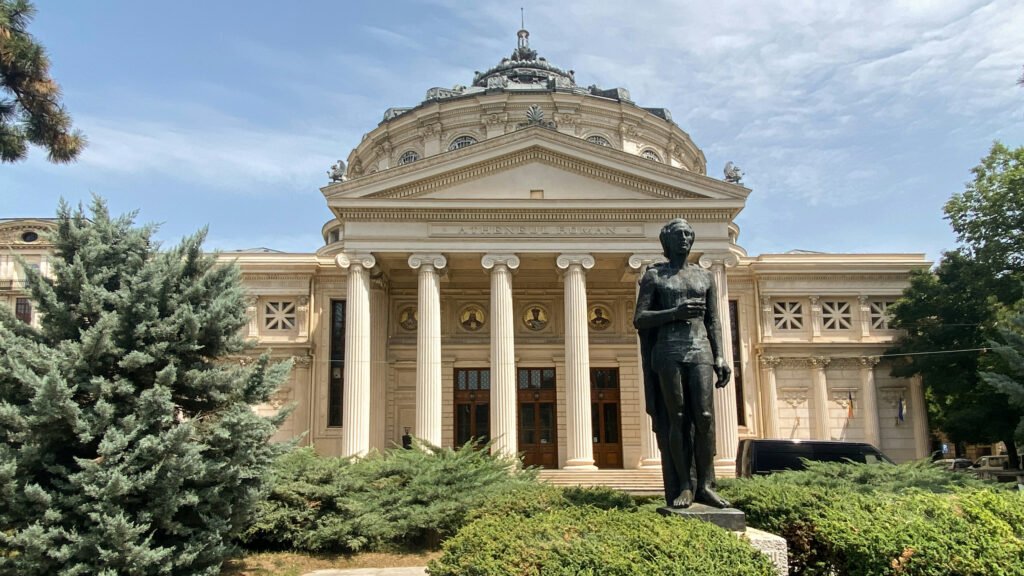 Neoclassical Romanian Athenaeum with a domed roof, Corinthian columns, and a bronze statue in Bucharest, Romania.