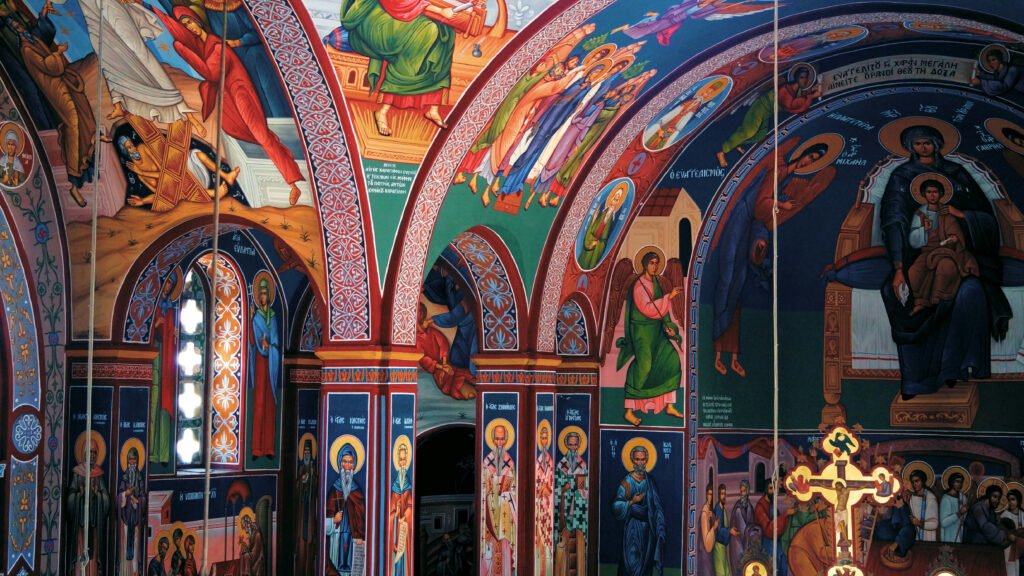 Colorful frescoes of saints, angels, and biblical scenes on arched ceilings and walls inside a painted monastery in Bucovina, Romania.