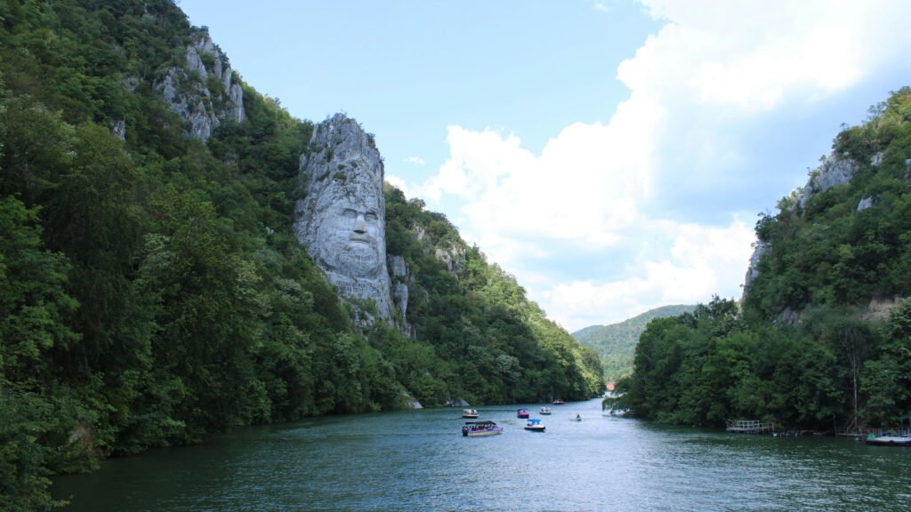 Rock sculpture of Decebalus carved into a limestone cliff along the Danube River, surrounded by forested mountains in the Iron Gates, Romania.