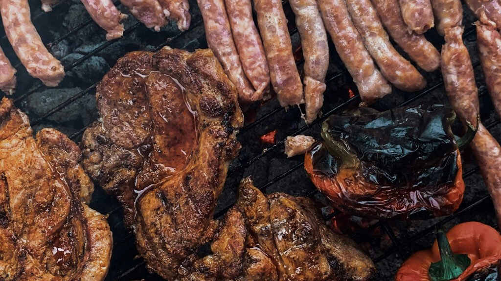 Grilled pork chops, mici sausages, and charred bell peppers on a barbecue grill in Romania, viewed from directly above.