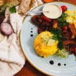 Traditional Romanian dish with polenta, slices of cured meat, cherry tomatoes, garlic, and fresh herbs on a blue ceramic plate.