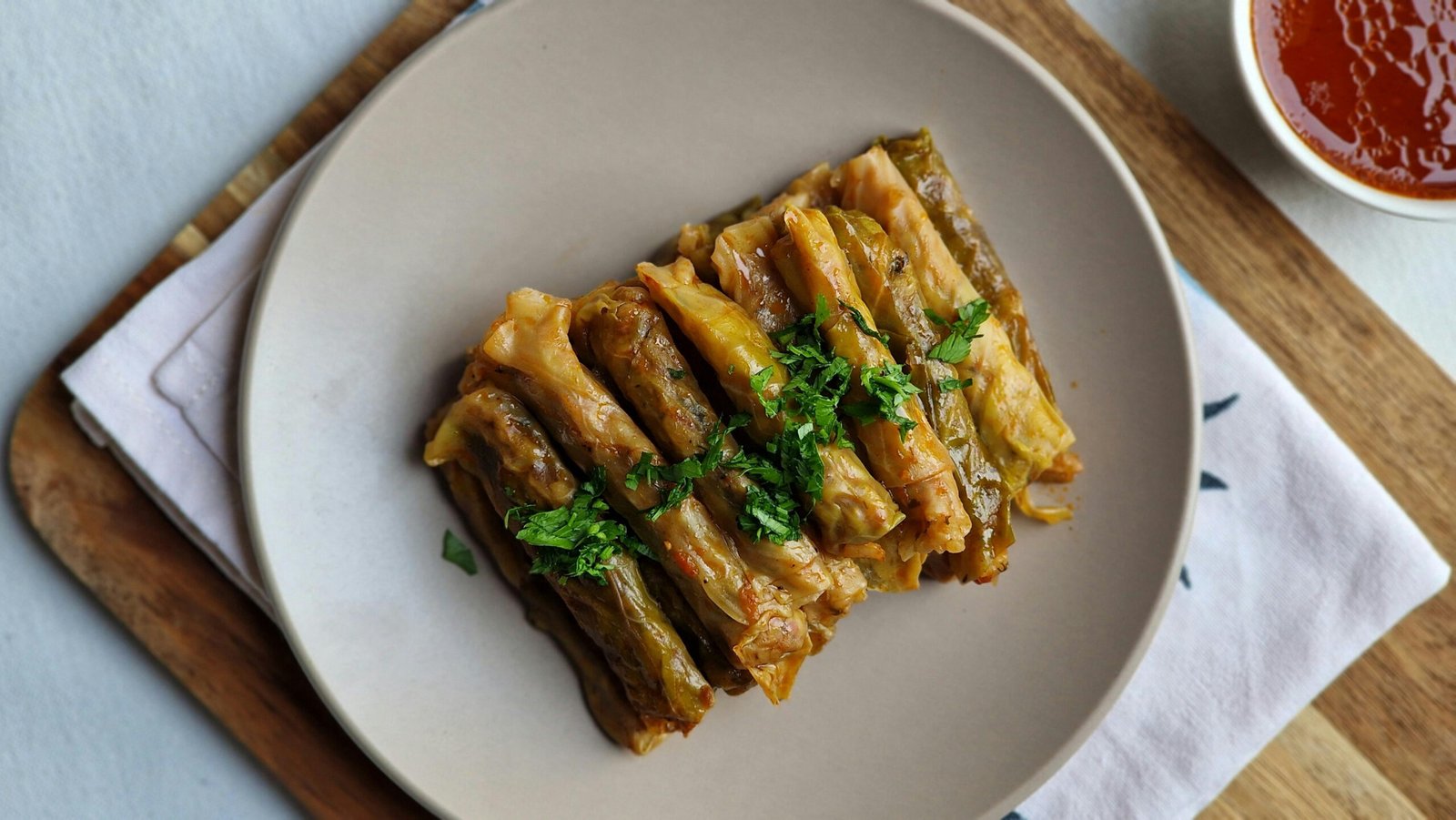 Plate of traditional Romanian sarmale, which are small cabbage rolls filled with seasoned meat and rice and garnished with fresh parsley on a neutral plate.
