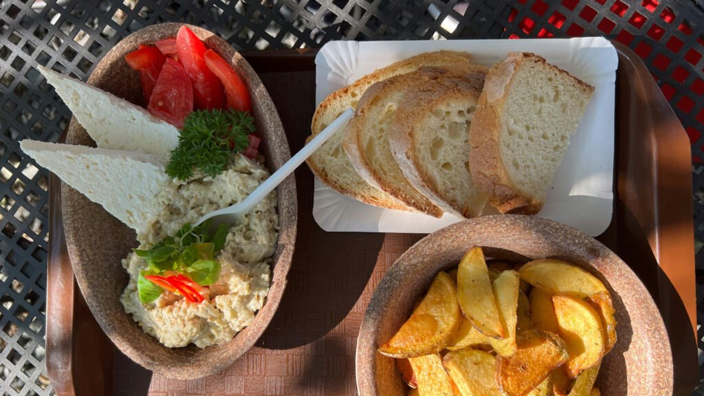 Top-down view of Romanian eggplant salad (salată de vinete) served with white cheese, sliced tomatoes, crusty bread, and roasted potatoes.