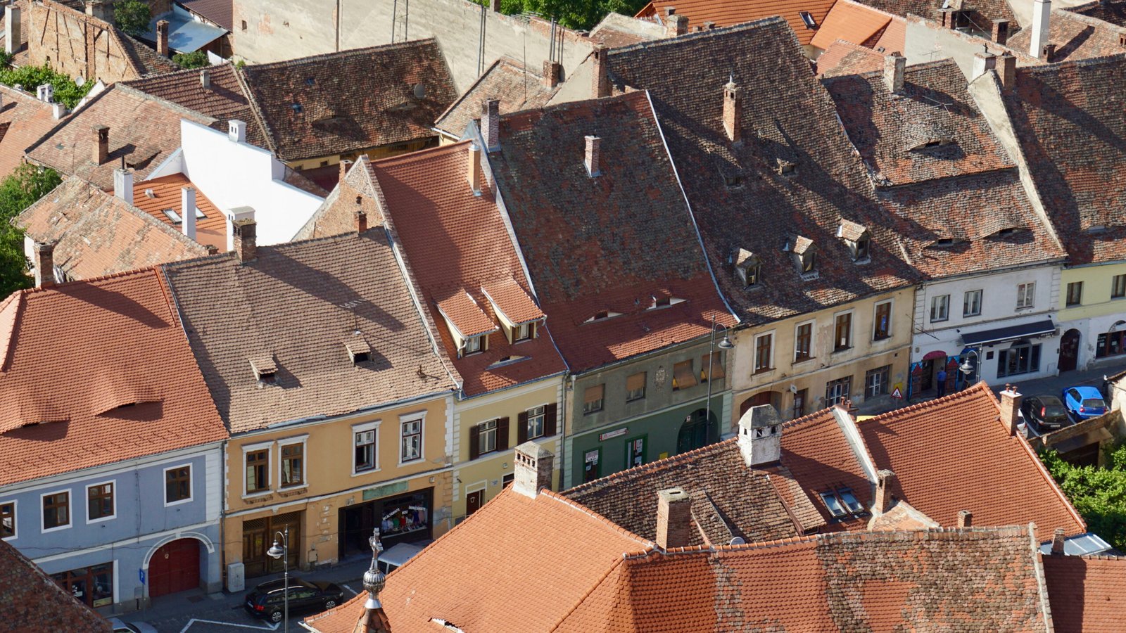 Tall narrow houses with steep tiled roofs and eyebrow dormers, located in Sibiu, Romania, seen from above on a sunny day.