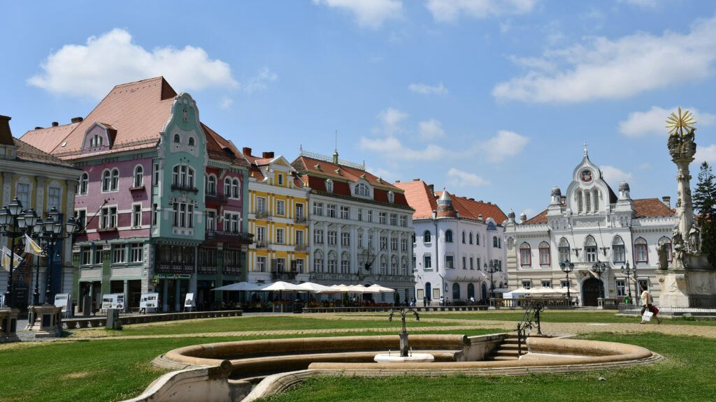 Historic buildings with colorful facades and baroque architecture surrounding Union Square with a fountain and monument in Timisoara, Romania.